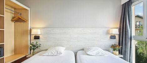 Quarto de hotel com duas camas, guarda-roupa de madeira, abajures e janela com cortinas.