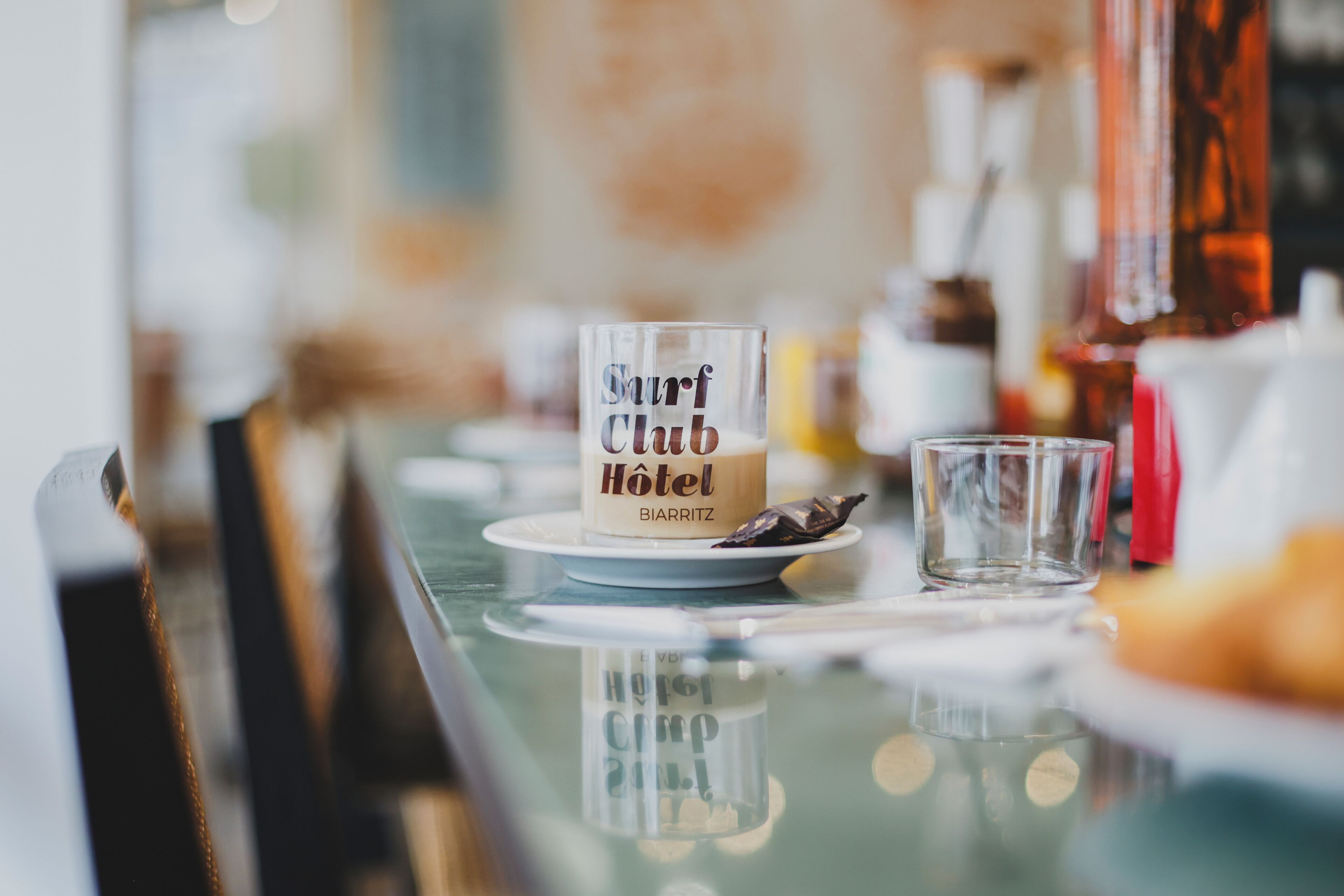 A bar setting with a glass table, a glass with a label reading 'Shirt Club Hotel,' and a small glass of water.