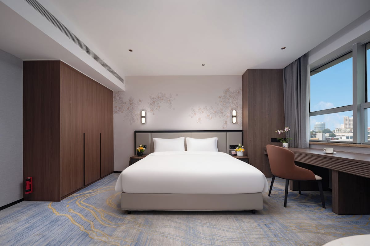 A modern hotel room with a large bed, a desk, and a view of the city.