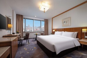 A hotel room with a large bed, a desk, a chair, a small table with flowers, and a window with a city view. - Liuhua Hotel (Guangzhou)
