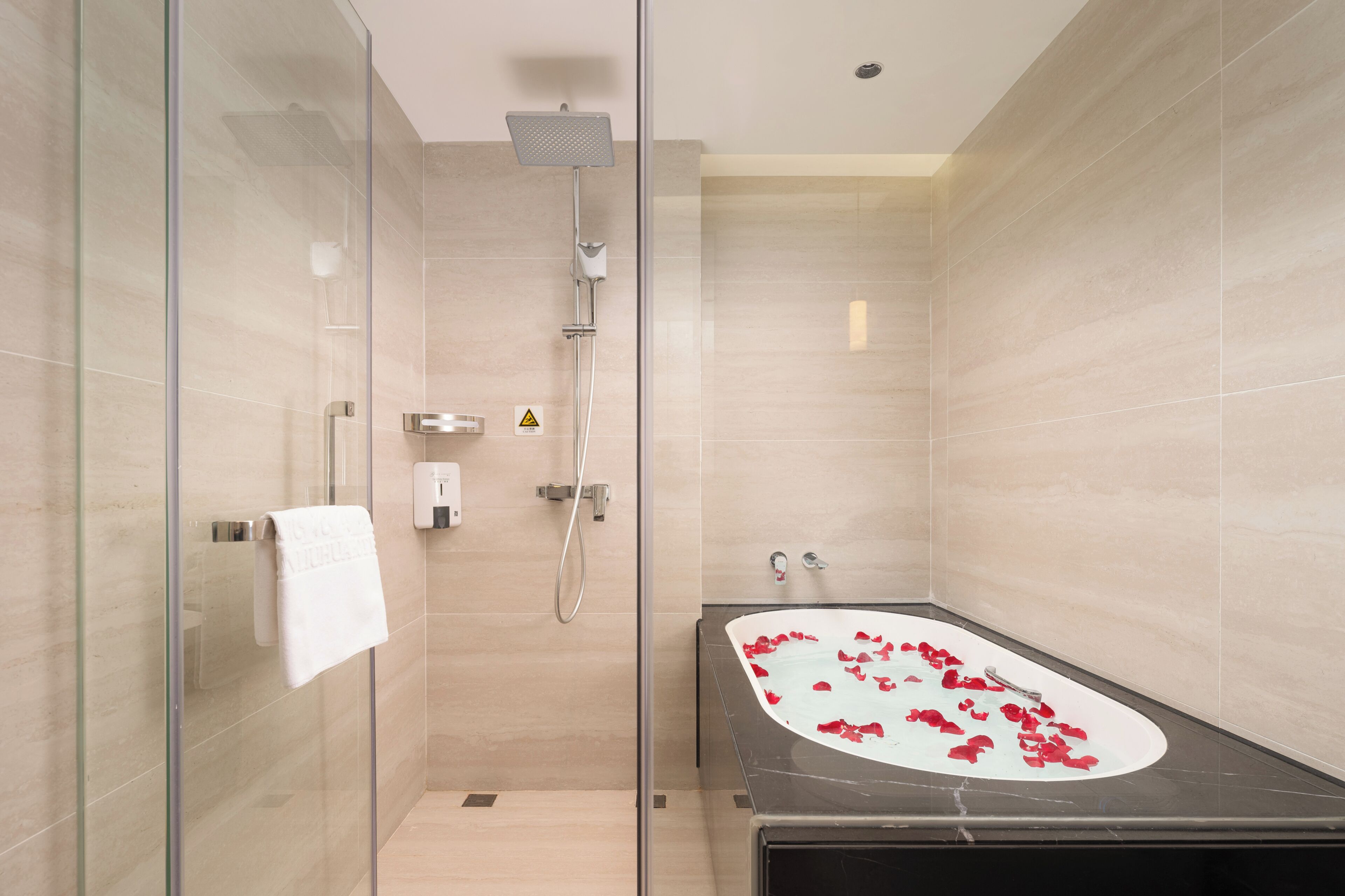 Un baño moderno con ducha de vidrio, una bañera independiente con pétalos de rosa y un perchero para toallas.