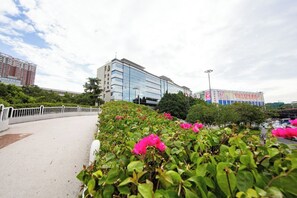 A pathway with a white fence, a building with reflective glass windows, and pink flowers in the foreground. - Liuhua Hotel (Guangzhou)