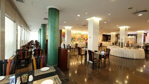 A spacious dining area with multiple tables and chairs, large pillars, and a colorful mural in the background. - Liuhua Hotel (Guangzhou)
