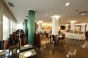A spacious dining area with multiple tables and chairs, large pillars, and a colorful mural in the background.