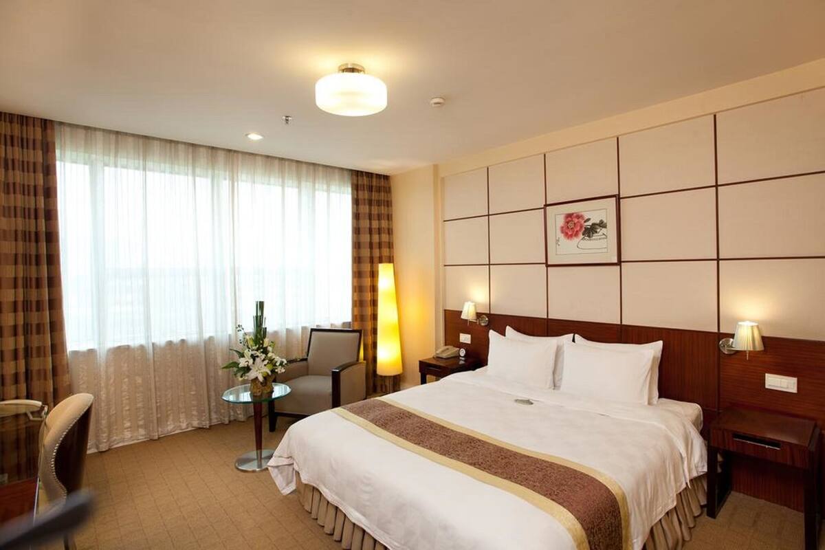 A hotel room with a large bed, a desk, a chair, a lamp, and a window with curtains.