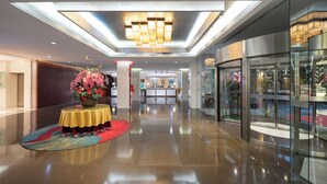 A modern hotel lobby with a polished floor, a central round table with a floral arrangement, and a glass elevator. - Liuhua Hotel (Guangzhou)