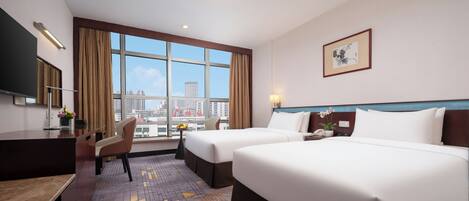 A hotel room with two beds, a desk, a chair, a TV, and a large window with a city view.