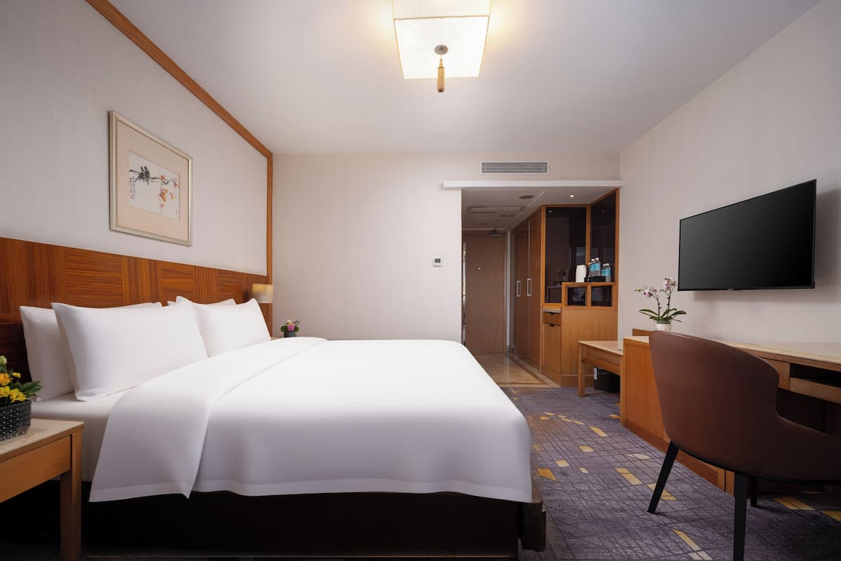 A hotel room with a bed, a desk, a chair, a television, and a framed picture on the wall.