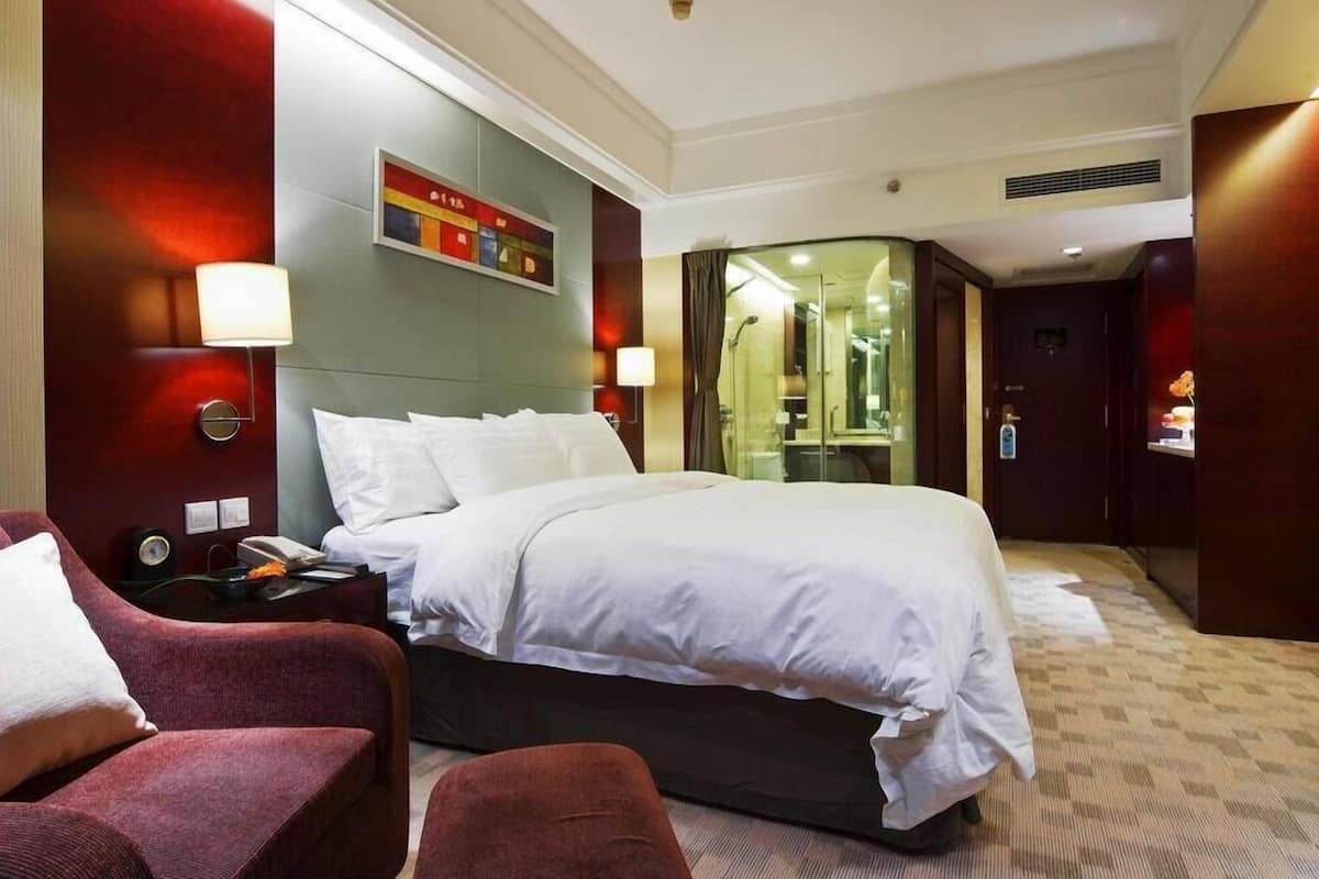 A hotel room with a large bed, a desk with a lamp, a chair, and a mirror.