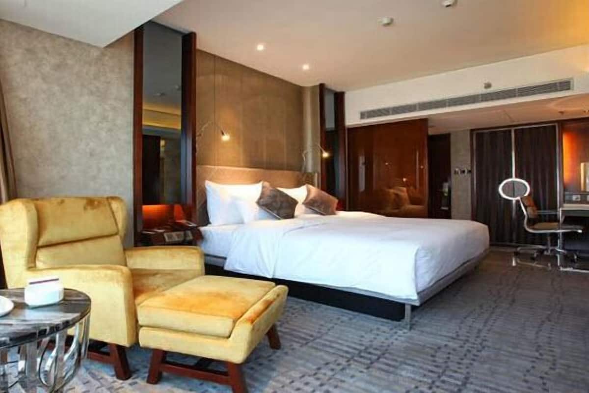 A hotel room with a bed, a chair, a desk, and a mirror.