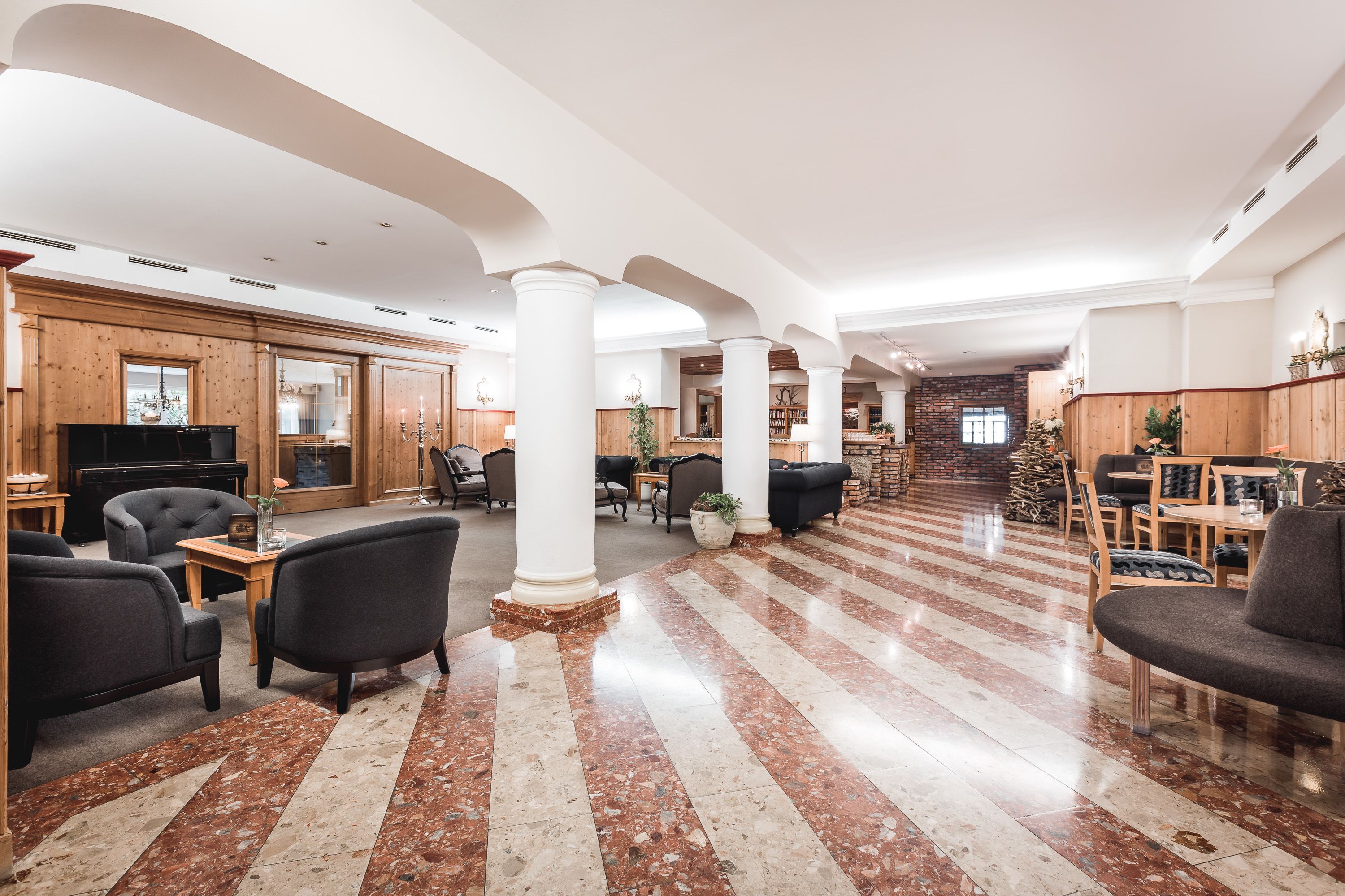 A spacious lobby with a high ceiling, marble flooring, and a central seating area with sofas and armchairs.