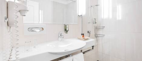 Un baño moderno con lavamanos, espejo y ducha blancos.