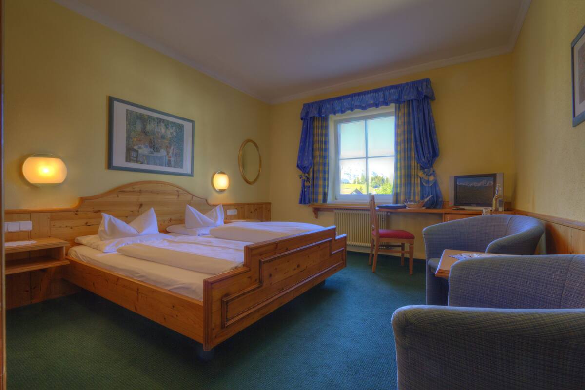 Una habitación de hotel con una cama de madera, un escritorio con una computadora, una silla y un ventanal con cortinas.
