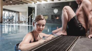 Una piscina interior con un diseño moderno, que incluye un techo de madera y una pared de piedra con un elemento decorativo.