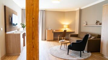 Un salon moderne avec un plancher en bois, une table basse ronde, un fauteuil noir, un canapé, un bureau avec une lampe et un miroir au mur.