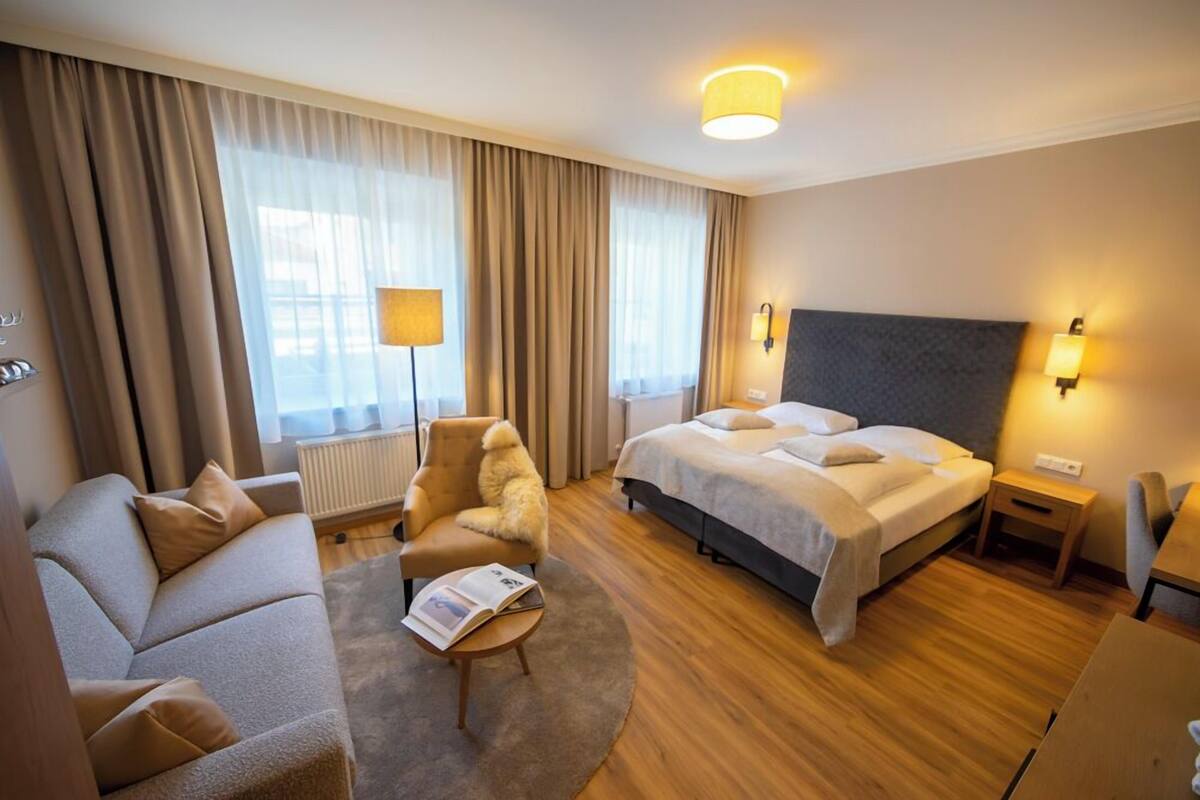 Una habitación de hotel con cama, sofá, sillón, lámpara y mesita de noche.
