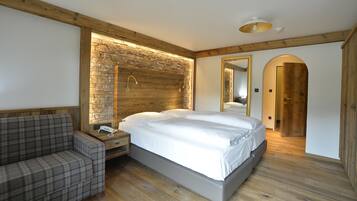 Een moderne slaapkamer met een accentmuur van steen, een houten hoofdbord, een groot bed, een nachtkastje met een telefoon en een geruite bank.
