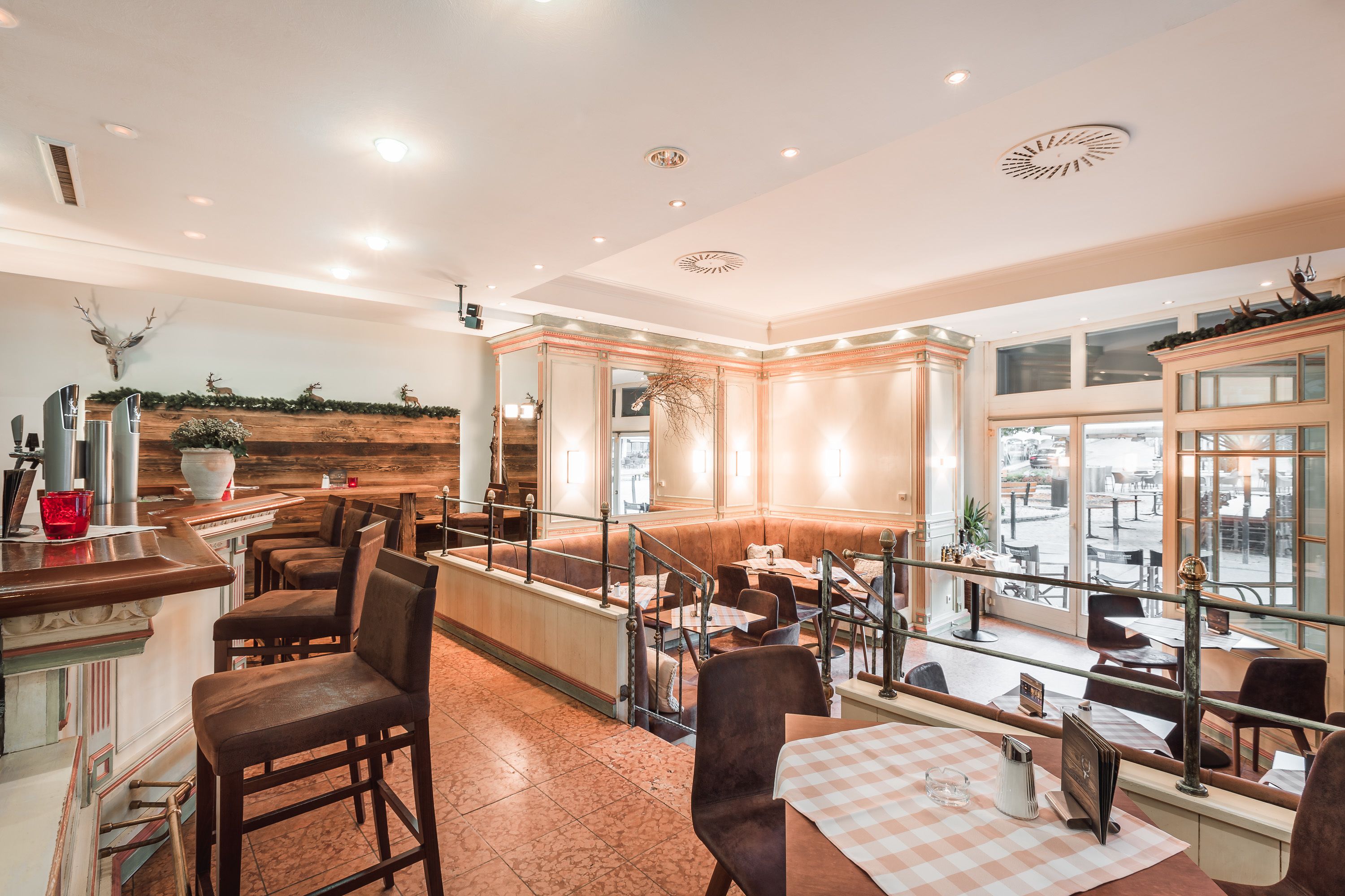 A restaurant with a high ceiling, recessed lighting, and a view of the street through large windows.