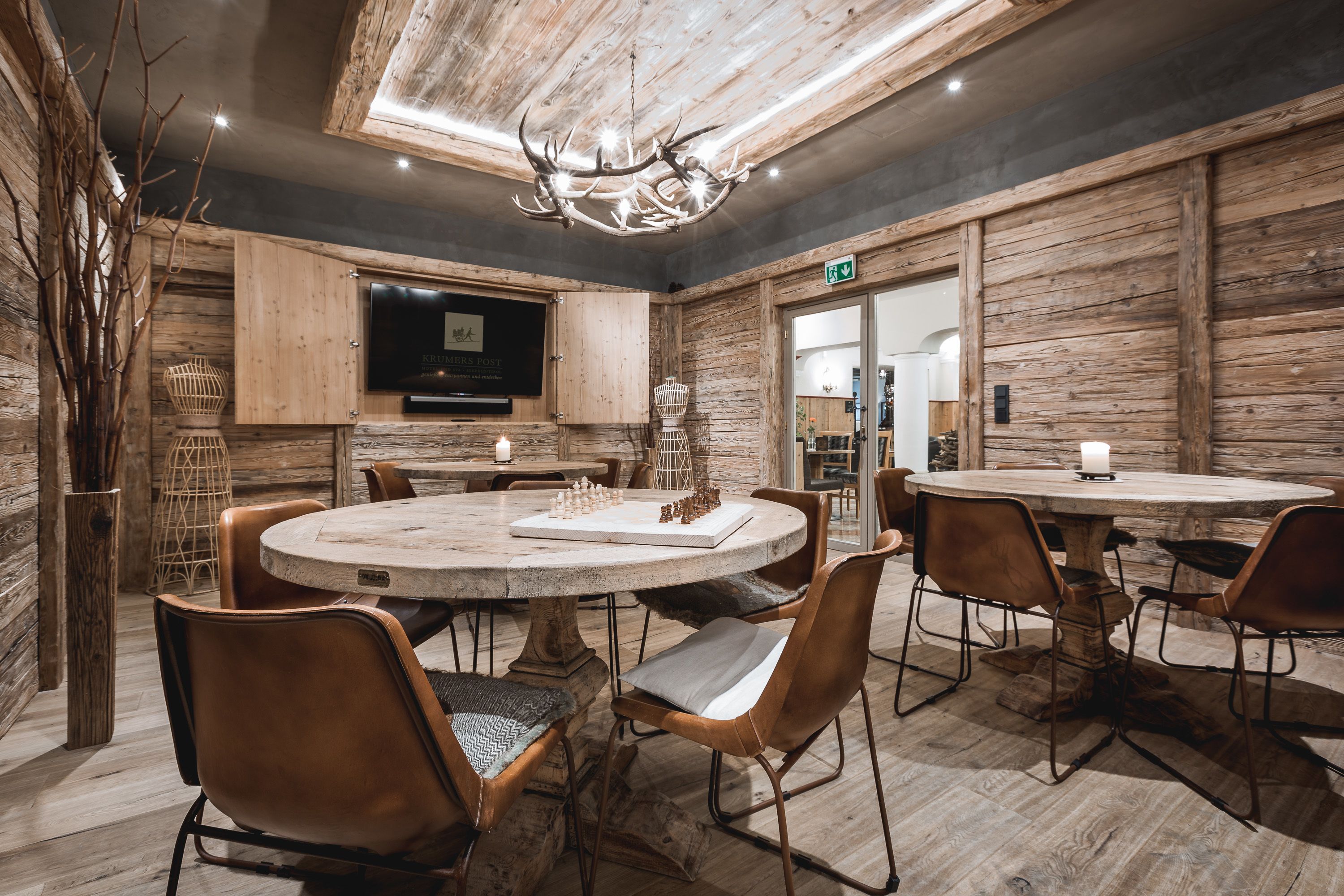 A rustic dining area with wooden walls, a chandelier, and a round table with chairs.
