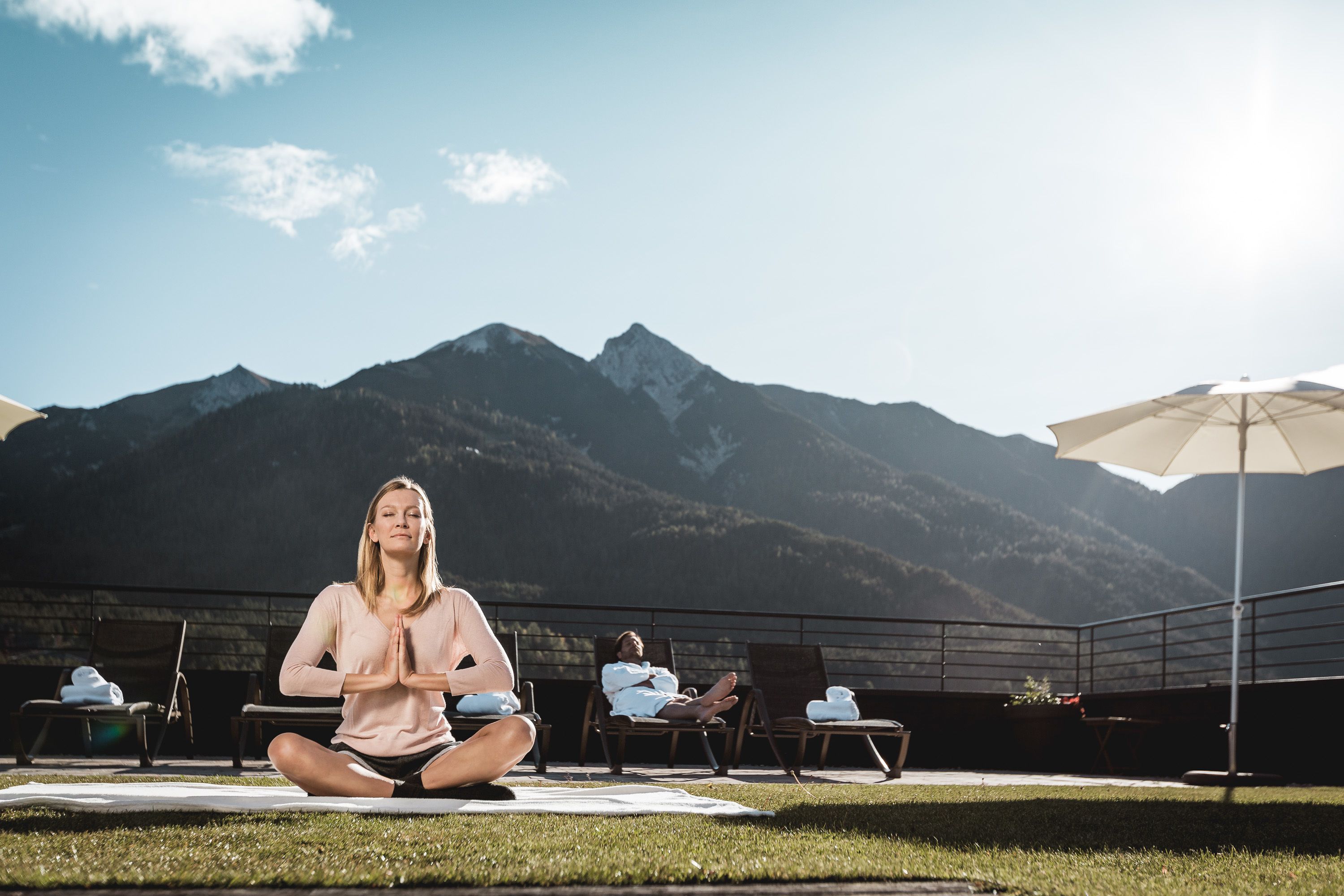 A person meditating on a mat outdoors with mountains in the background.