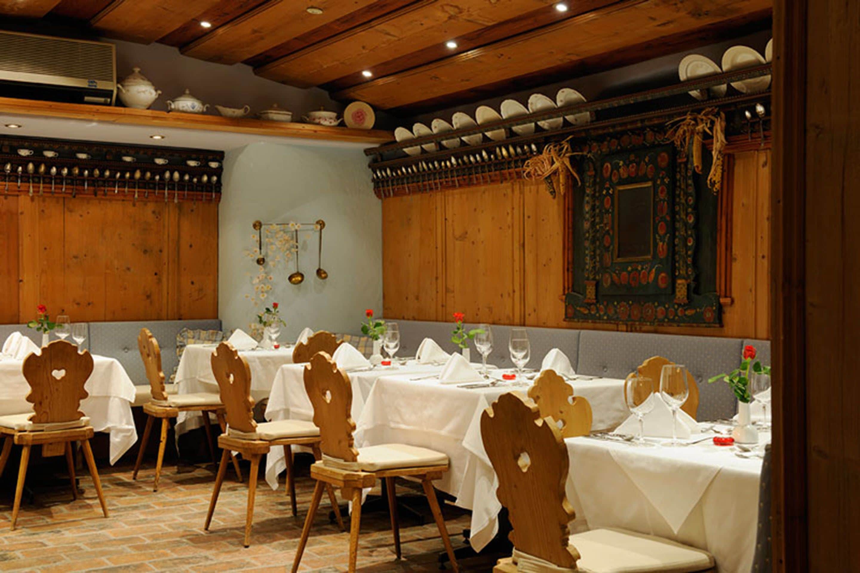 A dining area with wooden tables and chairs, white tablecloths, and a decorative mirror on the wall.