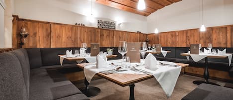 A restaurant with wooden panel walls, dark grey upholstered seating, and tables set with white tablecloths and silverware.