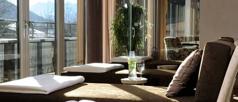 A sunlit room with a sofa, a small table with a bottle and glass, and a chair.