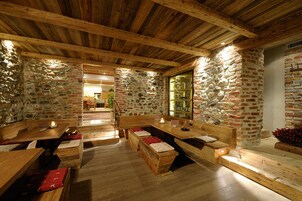 Un interior rústico con vigas de madera y paredes de piedra, que incluye bancos y mesas de madera.
