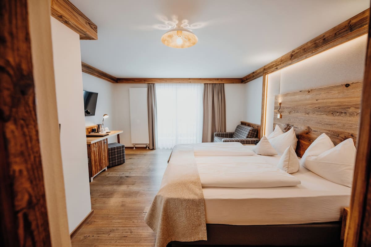 Habitación de hotel con cabecera de madera, cama con ropa blanca, escritorio con lámpara y televisor en la pared.
