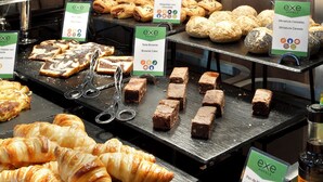 Un bufé con diversas opciones de panadería y repostería, incluyendo croissants, mini pasteles y brownies, con sus nombres identificados.