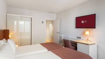 A hotel room with a bed, a desk, a chair, a television, and a radiator.