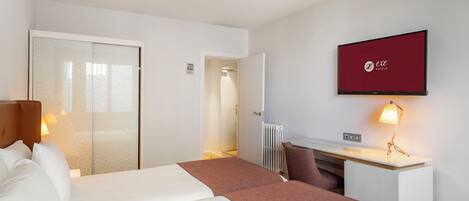 A hotel room with a bed, a desk, a chair, a television, and a radiator.