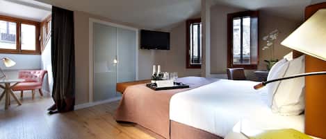 Habitación de hotel con una cama grande, un escritorio con lámpara, una silla, un televisor y un ventanal con cortinas.