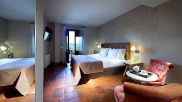 Ein Hotelzimmer mit zwei Betten, einer Sitzecke mit einem Sessel, einem kleinen Tisch mit Tablett und einem an der Wand montierten Fernseher.