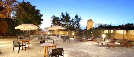 An outdoor patio area with stone flooring, tables, chairs, and umbrellas.