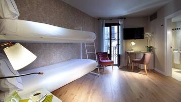 A room with a bunk bed, a desk with a chair, a lamp, a vase with flowers, and a window with curtains.