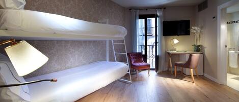 A room with a bunk bed, a desk with a chair, a lamp, a vase with flowers, and a window with curtains.