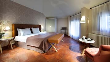 Habitación de hotel con cama, banca, silla, mesita de noche, lámpara y vista al exterior a través de cortinas.