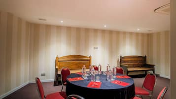 Un salón de conferencias con una mesa redonda, sillas rojas, un banco de madera y papel tapiz a rayas.