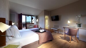 Habitación de hotel con cama, escritorio, silla, televisor y vistas al exterior.