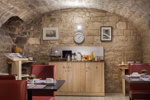 A rustic stone-walled dining area with wooden cabinets, a clock, and framed pictures. - Le Compostelle Le Marais (Paris)