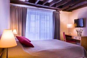 A hotel room with a bed, a desk, a chair, a TV, and a window with curtains. - Le Compostelle Le Marais (Paris)