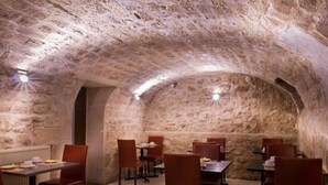 Ένας υπόγειος χώρος εστίασης με πέτρινους τοίχους και τραπέζια στρωμένα για φαγητό.