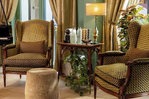 A room with two patterned armchairs, a small table with a lamp, and a potted plant. - Le Relais Madeleine (Paris)