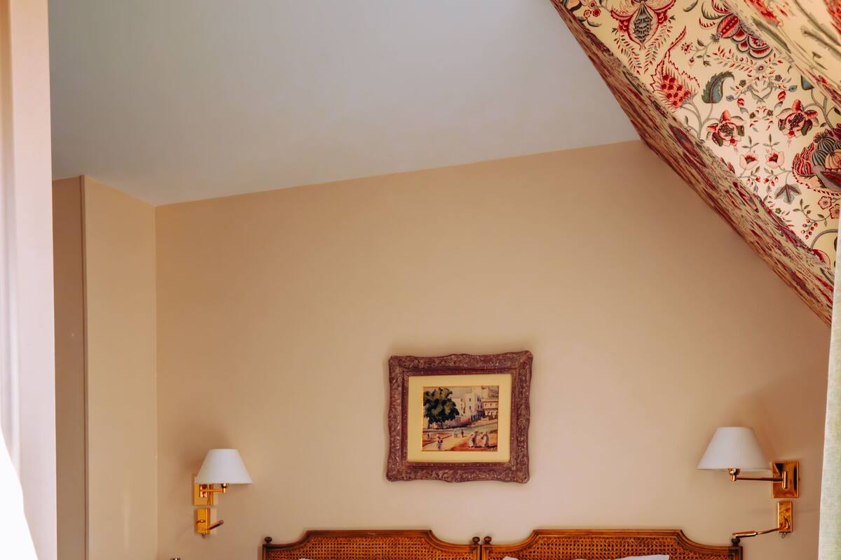 A hotel room with a large bed, two bedside tables, a nightstand, a framed picture on the wall, and a patterned curtain.