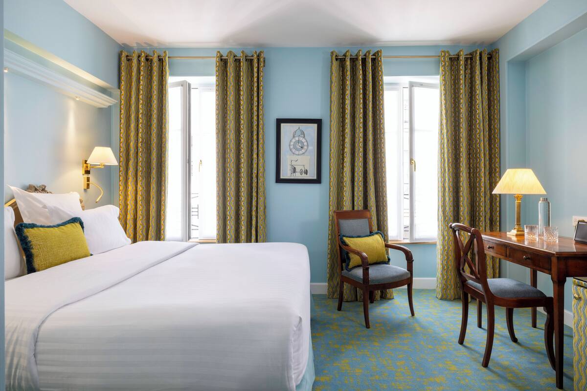 A hotel room with a large bed, two chairs, a desk, and curtains.