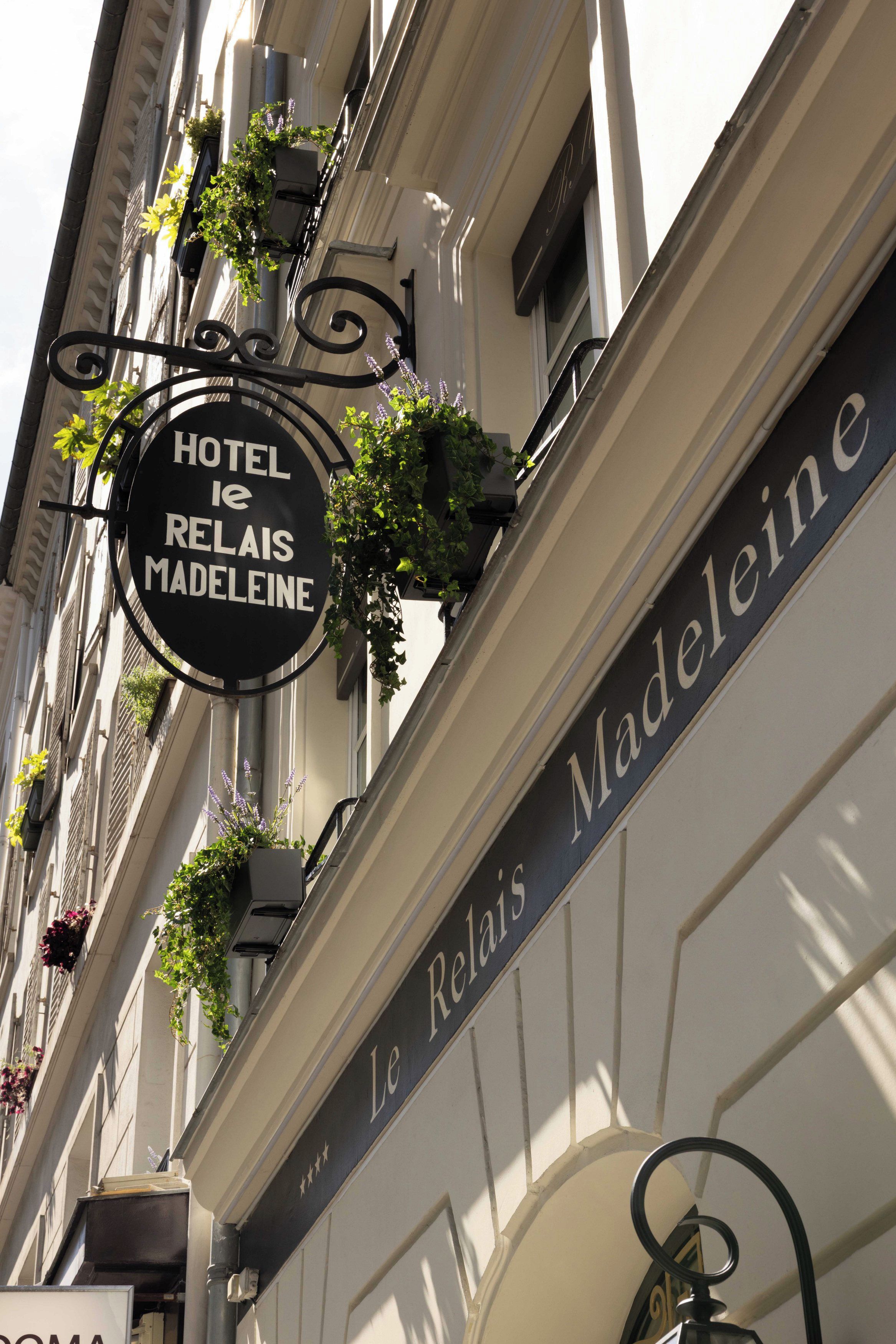 A hotel sign with 'HOTEL RELAIS MADELEINE' and a decorative ironwork sign above it.