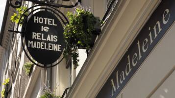 A hotel sign with 'HOTEL RELAIS MADELEINE' and a decorative ironwork sign above it.