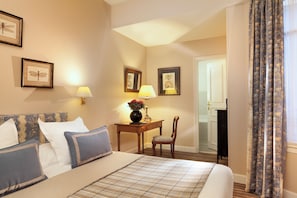 A hotel room with a bed, a desk with a lamp, and framed artwork on the walls. - Le Relais Madeleine (Paris)