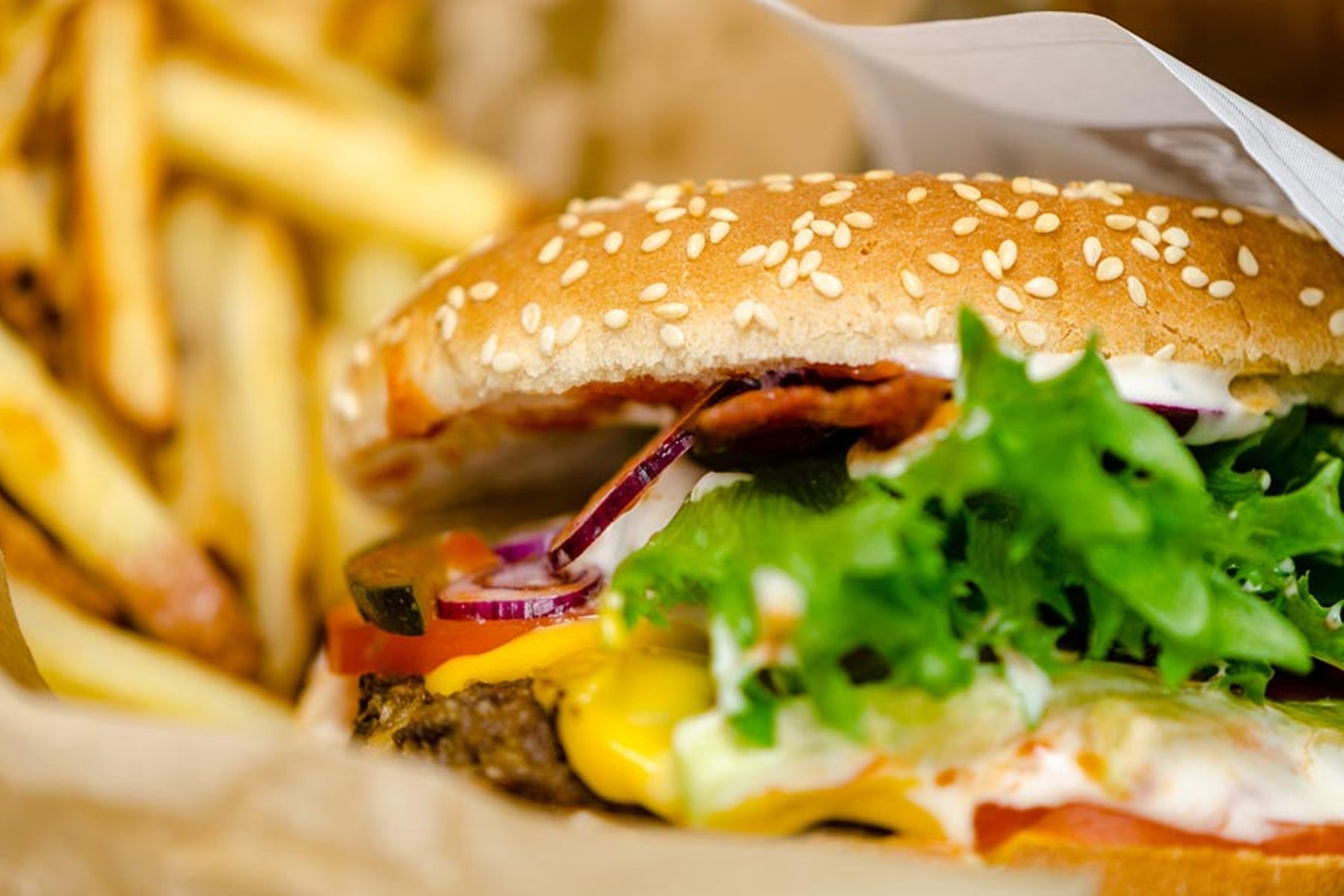 Close-up van een hamburger met sesamzaadbolletje, sla, kaas en een rundvleespatty, geserveerd met frieten.